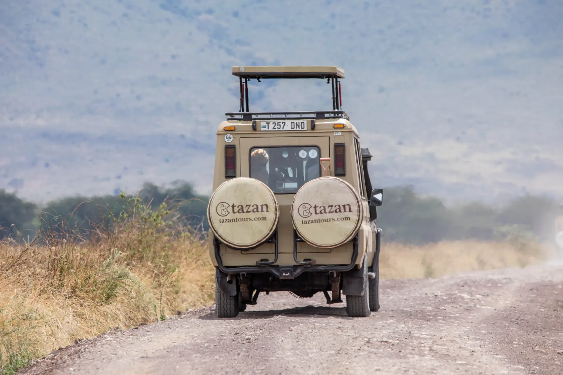 Tazan Tours safari vehicle driving a dirt road through the hills