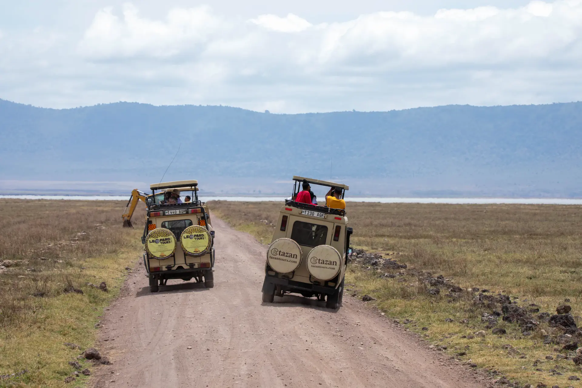 Two safari vehicles on a dirt road across the Ngorongoro Crater floor
