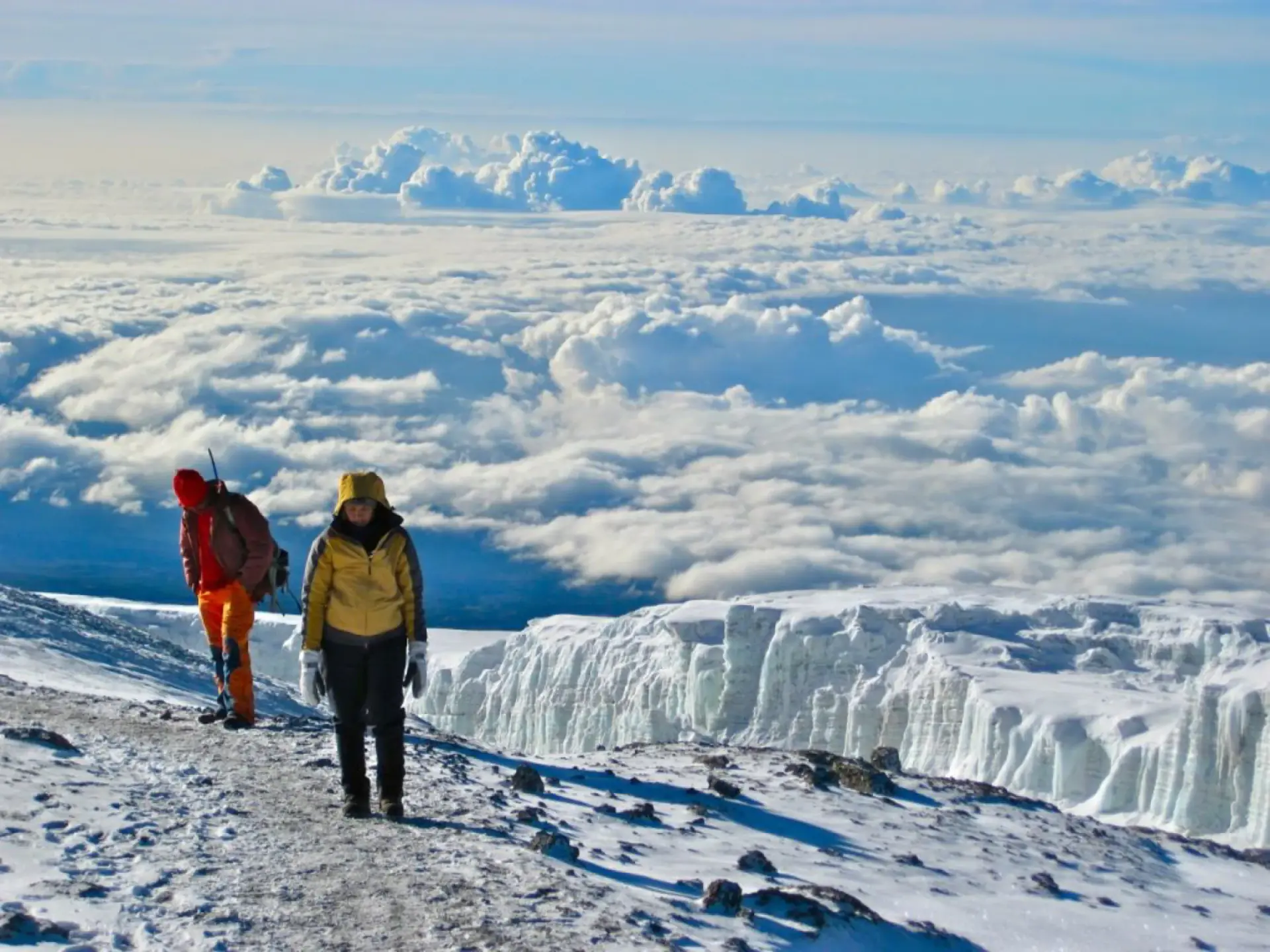 Two climbers walking beside a glacier high above the clouds