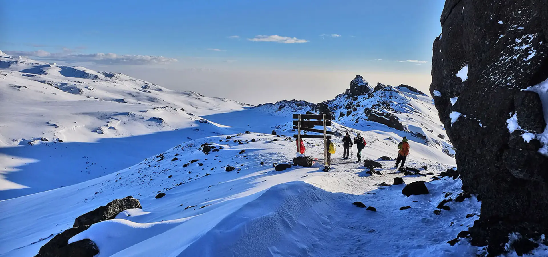 Climbers at the Uhuru Peak summit sign in the snow