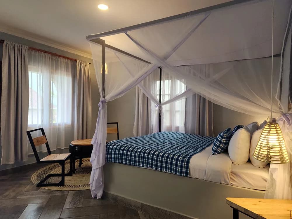 Four-poster bed with a blue checked throw in a sunlit suite at Heart & Soul Lodge