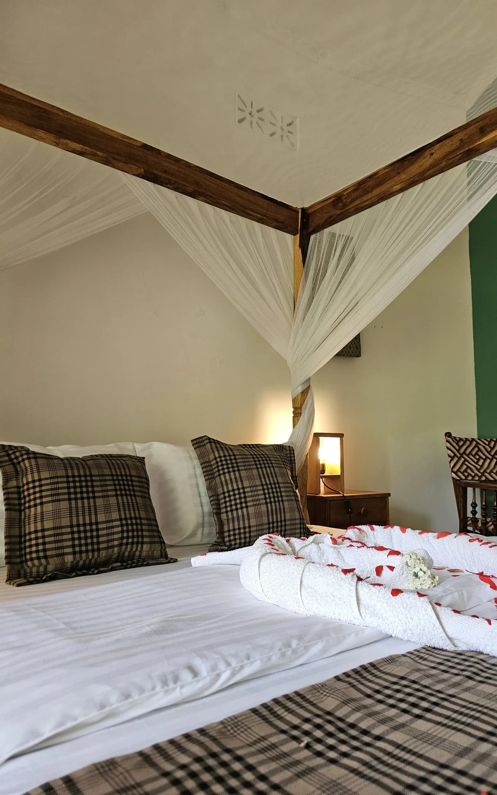 Netted four-poster bed with a towel decoration and rose petals at Ilboru Safari Lodge