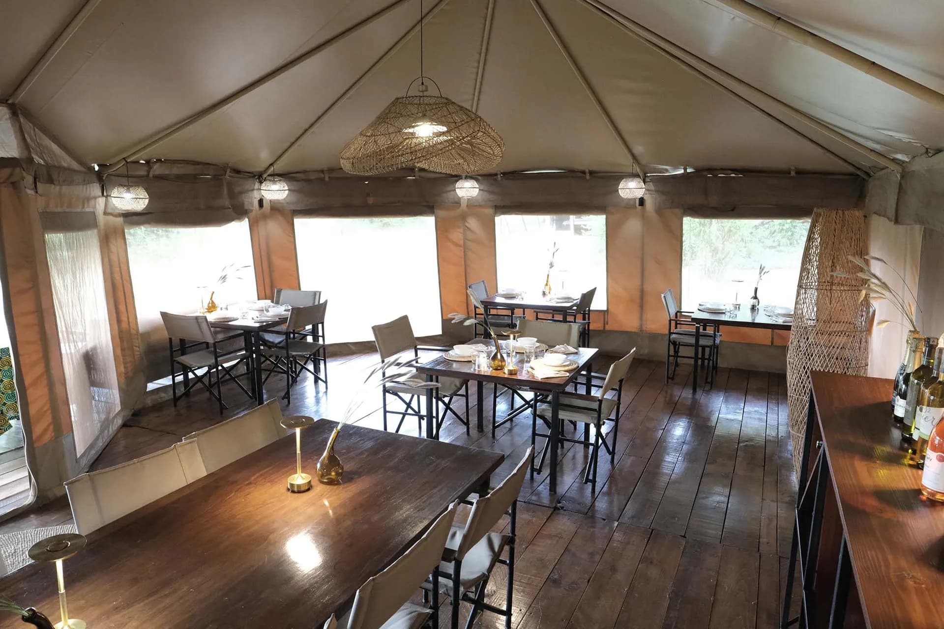 Dining tent at The Whisper Tarangire with wooden tables and woven lamps