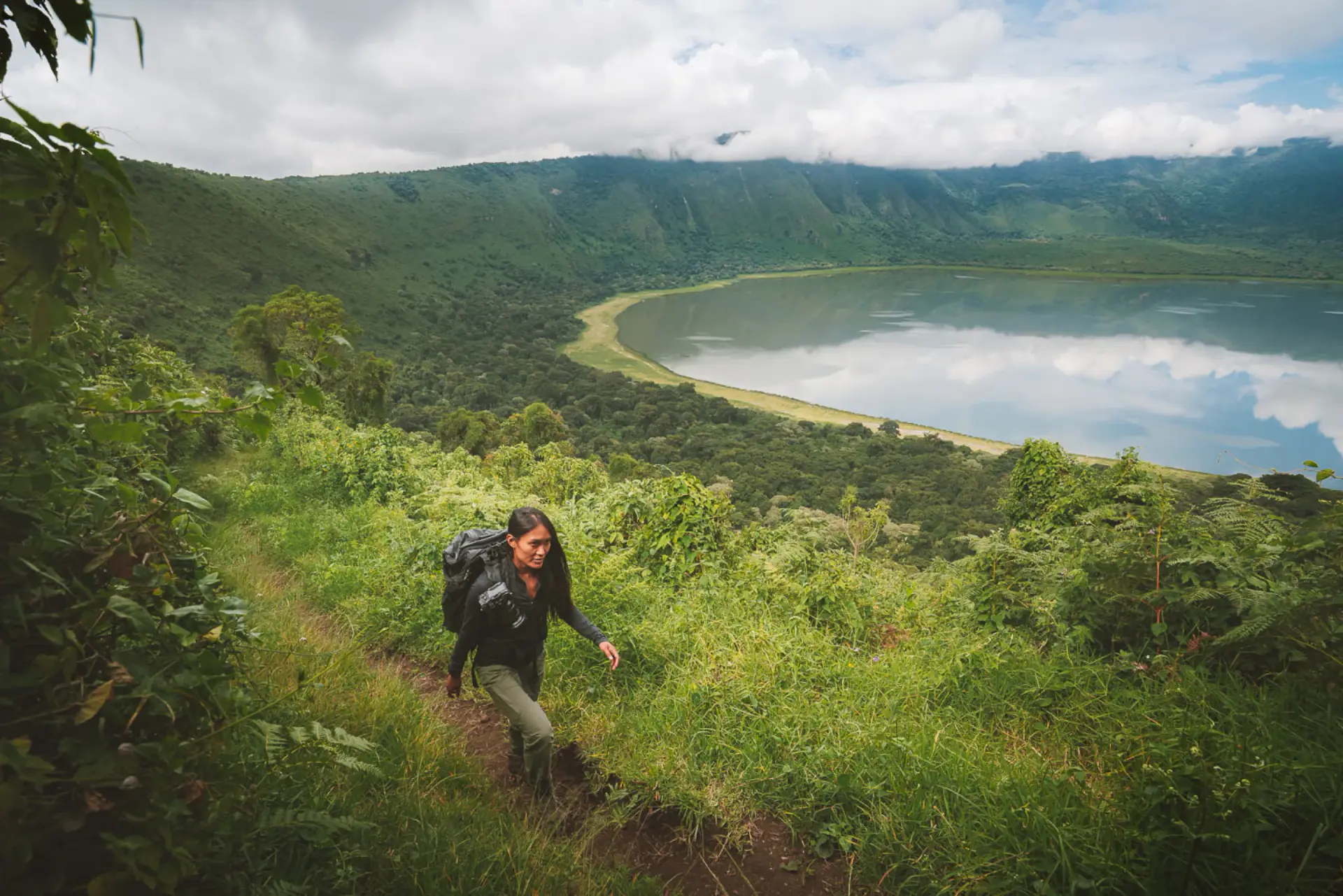 Hiker descending through green forest into the Empakaai Crater