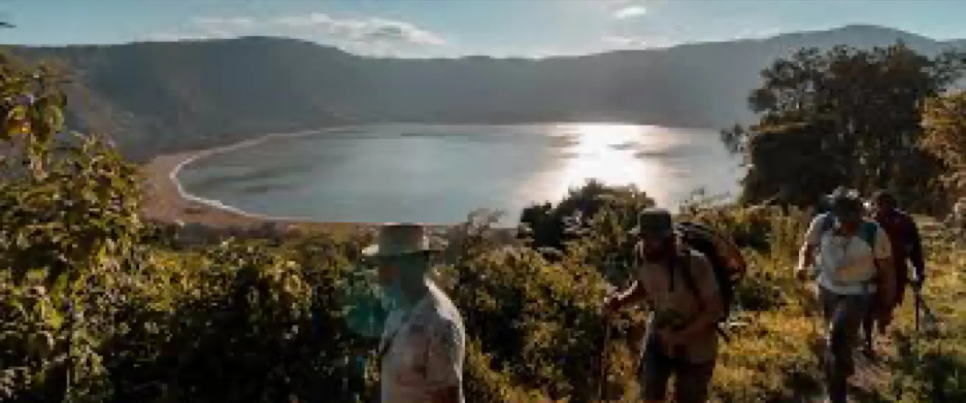Hikers on the crater rim above a sunlit lake