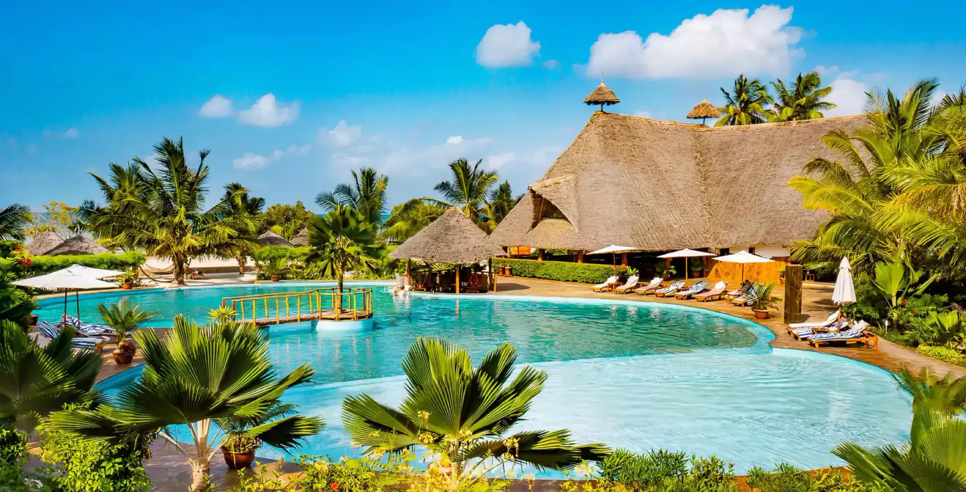 Resort swimming pool surrounded by palms and thatched roofs in Zanzibar